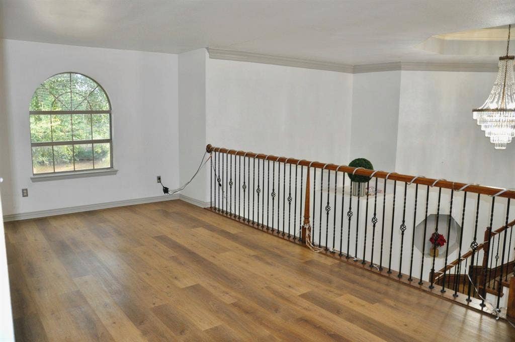 3620 Carlton Court, Sachse, TX 75048 Open space featuring arched window, wood-finish flooring, metal baluster railing with wood handrail, and crystal chandelier
