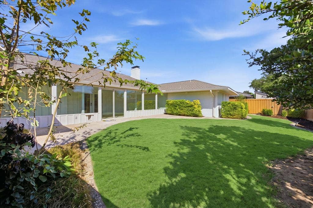 6978 Pemberton Drive, Dallas, TX 75230 Expansive backyard featuring a curved lawn, paved patio, mature landscaping, and an exterior brick chimney