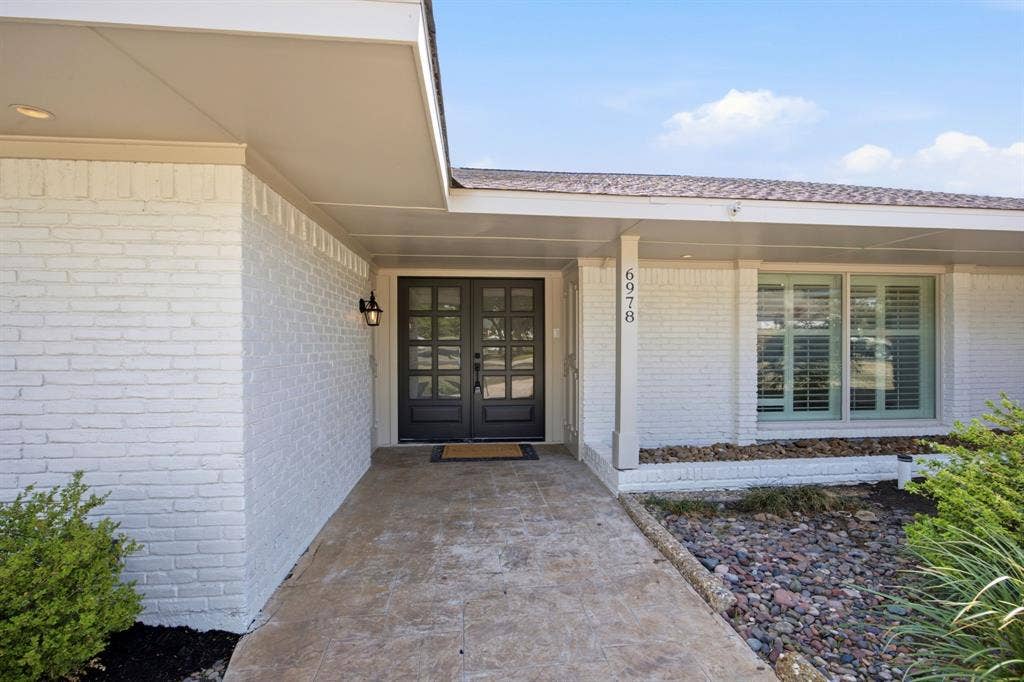 6978 Pemberton Drive, Dallas, TX 75230 Painted brick exterior featuring a covered porch, stone-finish walkway, double-entry doors with multi-pane glass, and window shutters