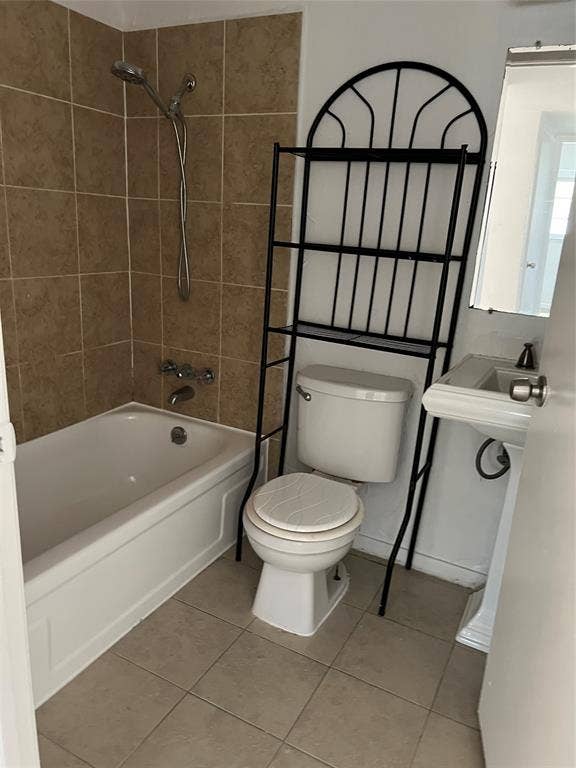 5005 Highridge Drive, Garland, TX 75043 Bathroom featuring a porcelain-finish bathtub, wall-mounted shower head, tiled tub surround, pedestal sink, and floor tiling