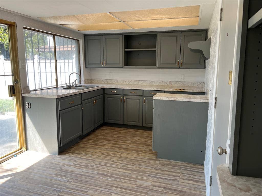 5005 Highridge Drive, Garland, TX 75043 Kitchen featuring charcoal-toned cabinetry, stone-finish countertops, wood-finish flooring, dual-basin stainless steel sink, and a glass sliding door