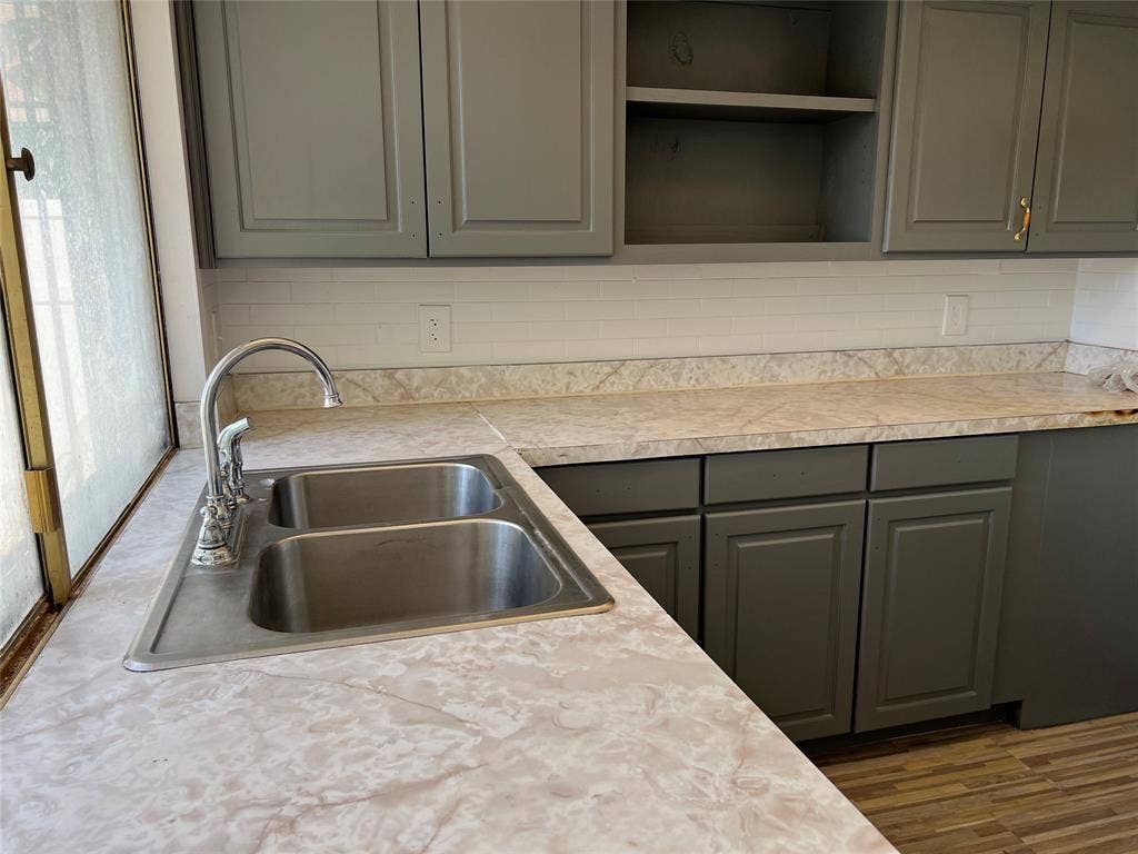 5005 Highridge Drive, Garland, TX 75043 Kitchen featuring gray cabinetry, stone-patterned laminate countertops, white subway tile backsplash, stainless steel double-basin sink, and high-arc faucet