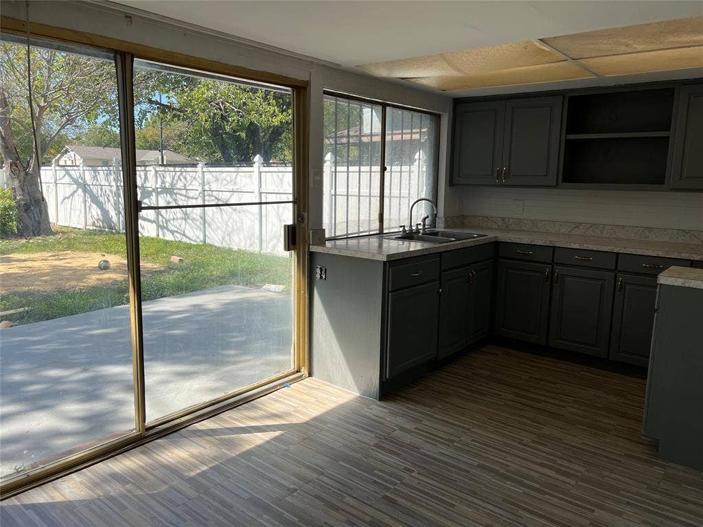 5005 Highridge Drive, Garland, TX 75043 Kitchen featuring dark-toned cabinetry, light-colored countertops, wood-finish flooring, and large sliding glass doors opening to a concrete patio