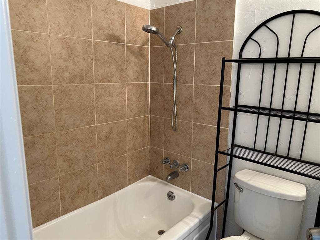 5005 Highridge Drive, Garland, TX 75043 Bathtub with porcelain surround, beige ceramic wall tiling, and adjustable handheld shower head with chrome fixtures