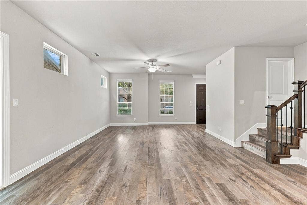 614 Ansley Way, Allen, TX 75013 Open-concept interior featuring wood-finish flooring, multi-pane windows, ceiling fan, and a staircase with dark wood handrails and metal balusters