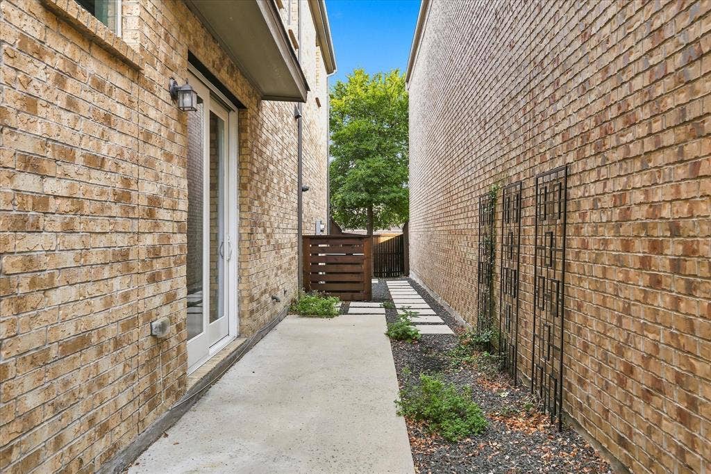 614 Ansley Way, Allen, TX 75013 Side exterior featuring a brick facade, concrete walkway, gravel landscaping, metal wall trellises, and wood-slat privacy fencing