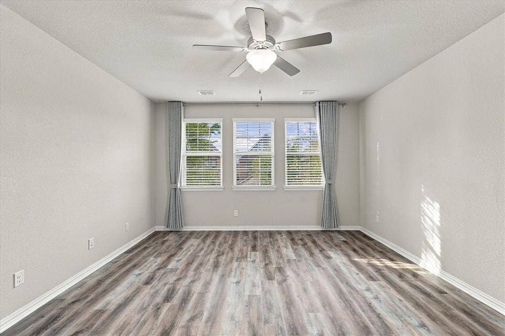 614 Ansley Way, Allen, TX 75013 Room featuring wood-finish flooring, three windows with horizontal blinds, and a central ceiling fan with an integrated light fixture