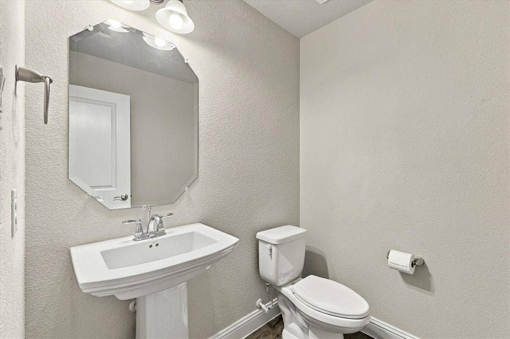 614 Ansley Way, Allen, TX 75013 Powder room featuring a white pedestal sink, chrome dual-handle faucet, octagonal wall-mounted mirror, and brushed-finish metal towel bar