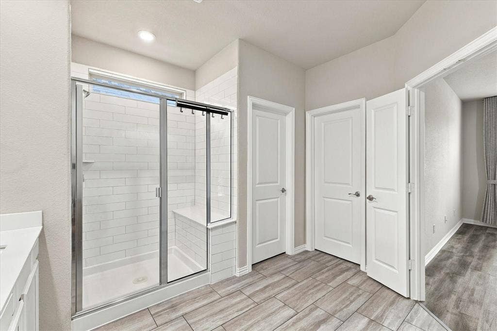 614 Ansley Way, Allen, TX 75013 Walk-in shower featuring a built-in tiled bench, white subway tile surround, and chrome-framed glass enclosure, complemented by wood-finish floor tiling
