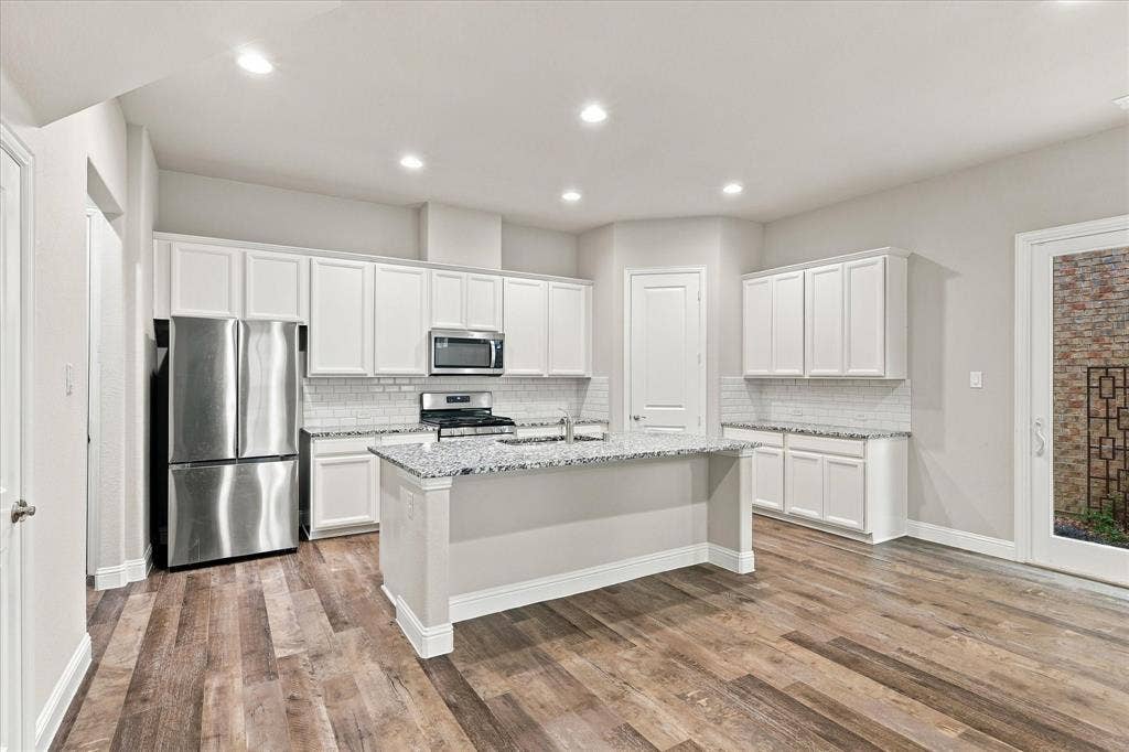 614 Ansley Way, Allen, TX 75013 Kitchen featuring white shaker-style cabinetry, stone-finish countertops, subway tile backsplash, stainless steel appliances, and wood-finish flooring