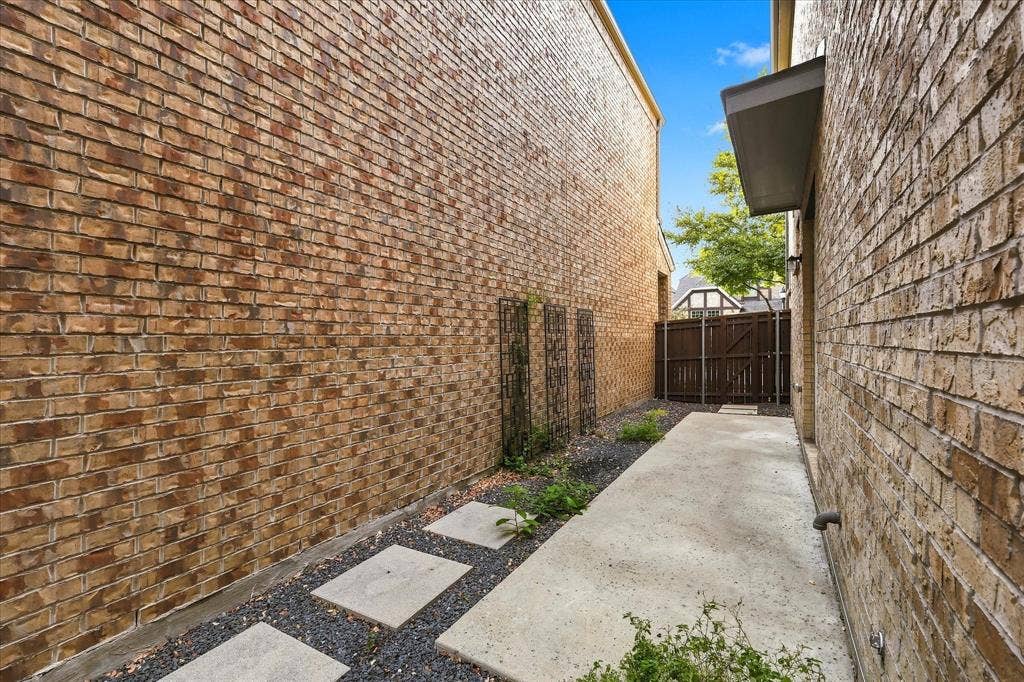 614 Ansley Way, Allen, TX 75013 Exterior side yard featuring full brick siding, concrete paver pathway, decorative metal wall trellises, and a wood privacy fence