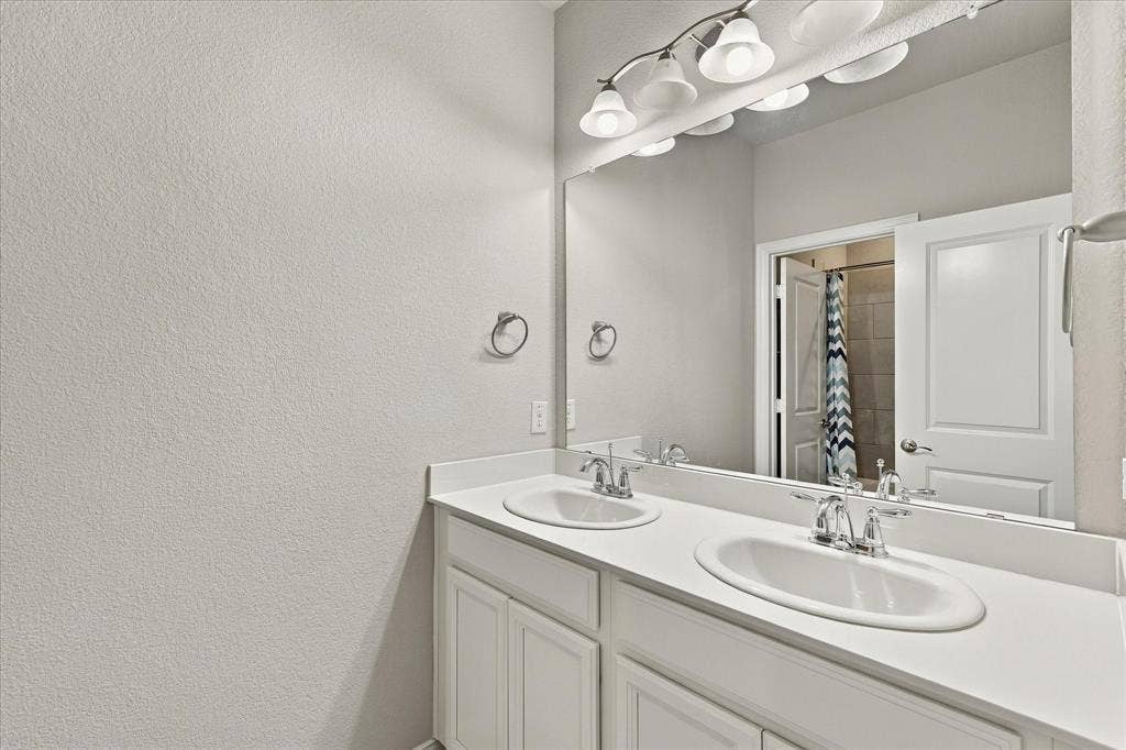 614 Ansley Way, Allen, TX 75013 Double vanity with white cabinetry, solid-surface countertop, dual drop-in sinks, polished chrome fixtures, and a wall-to-wall mirror
