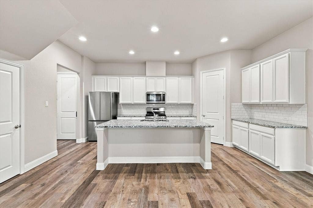 614 Ansley Way, Allen, TX 75013 Kitchen featuring white cabinetry, stone countertops, stainless steel appliances, a central island with an integrated sink, and wood-finish flooring