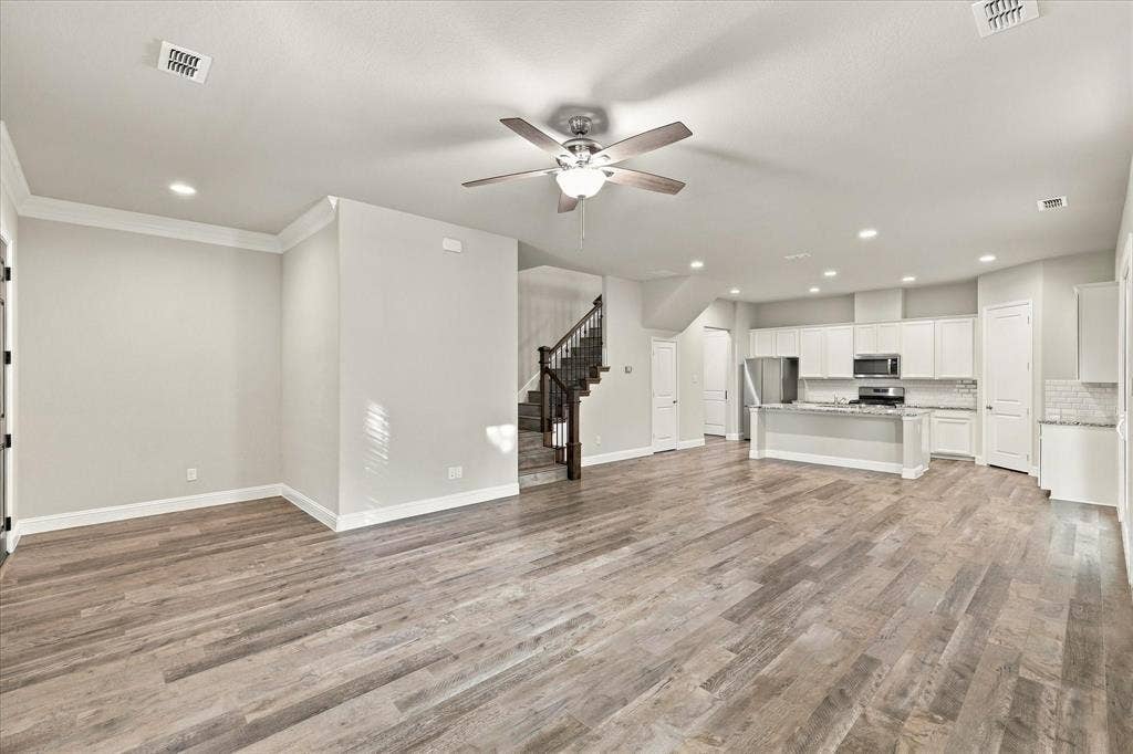 614 Ansley Way, Allen, TX 75013 Open-concept interior featuring wood-finish flooring, recessed lighting, a ceiling fan, white cabinetry with stone countertops, and a staircase with stained wood railings