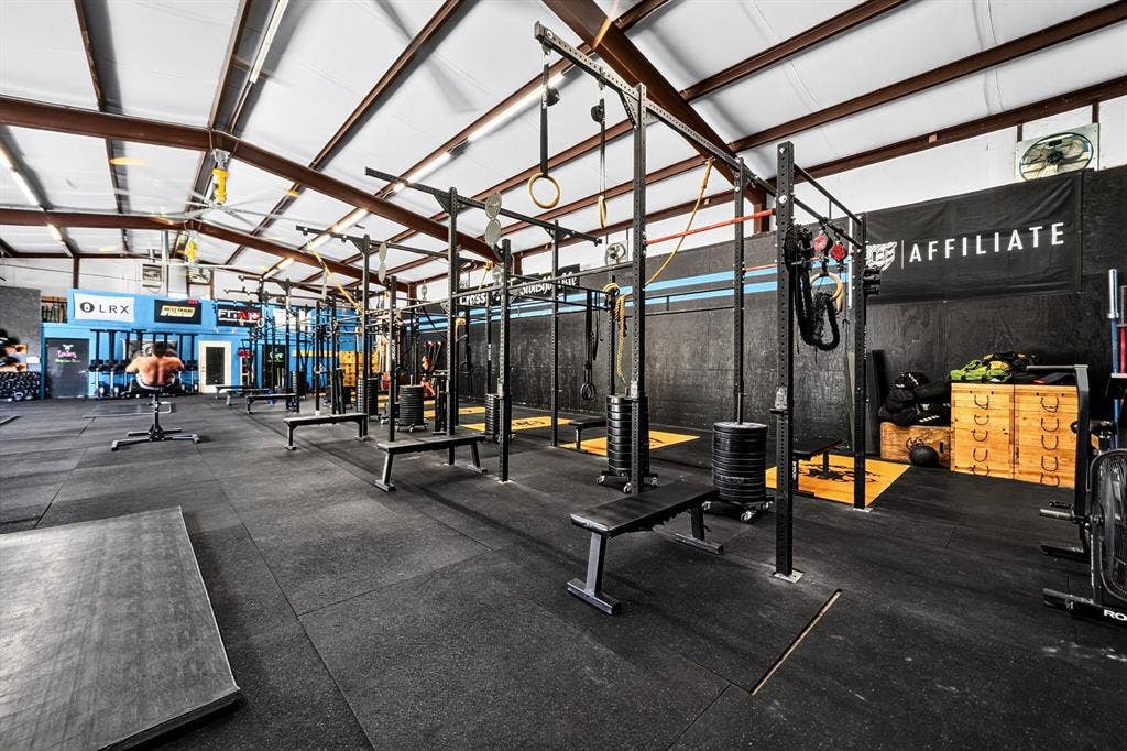911 W Holiday Drive, Fate, TX 75132 Open-concept fitness space featuring high-clearance vaulted ceilings with exposed steel beams, industrial lighting, durable rubberized flooring, and an expansive multi-station steel structural racking system