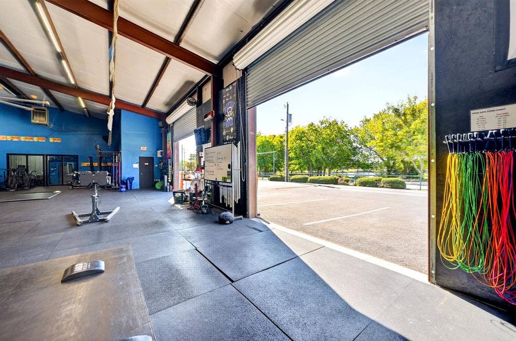 911 W Holiday Drive, Fate, TX 75132 Expansive open-concept space featuring industrial metal structural beams, high-clearance ceilings, durable rubber flooring, and a large-format roll-up door opening to a paved parking area