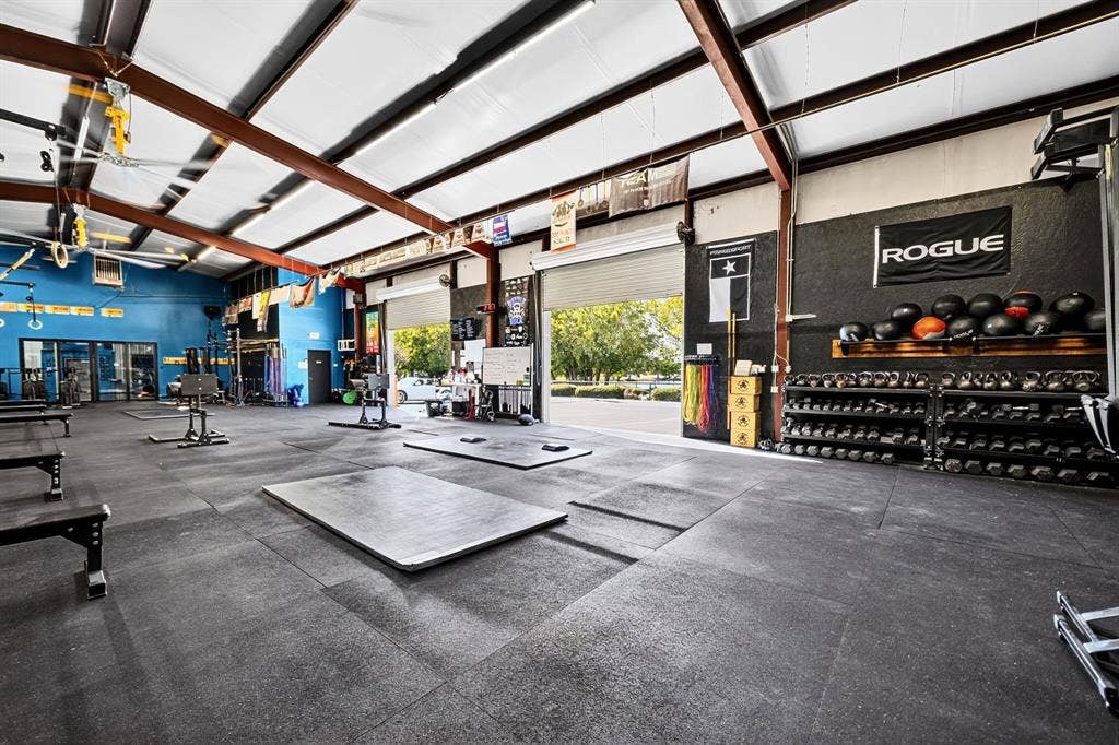 911 W Holiday Drive, Fate, TX 75132 Expansive open-concept utility space featuring exposed steel beam framing, high-clearance vaulted ceilings, industrial roller-style bay doors, and durable rubberized flooring