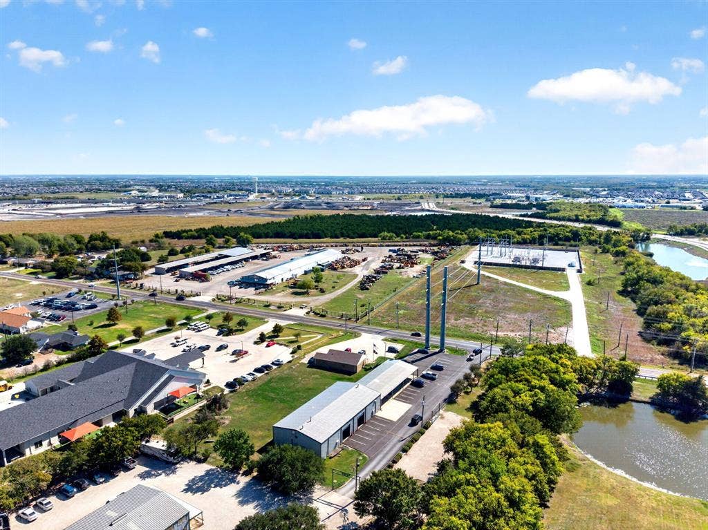 911 W Holiday Drive, Fate, TX 75132 Aerial perspective of a multi-structure property featuring paved parking areas, covered storage bays, and open land space