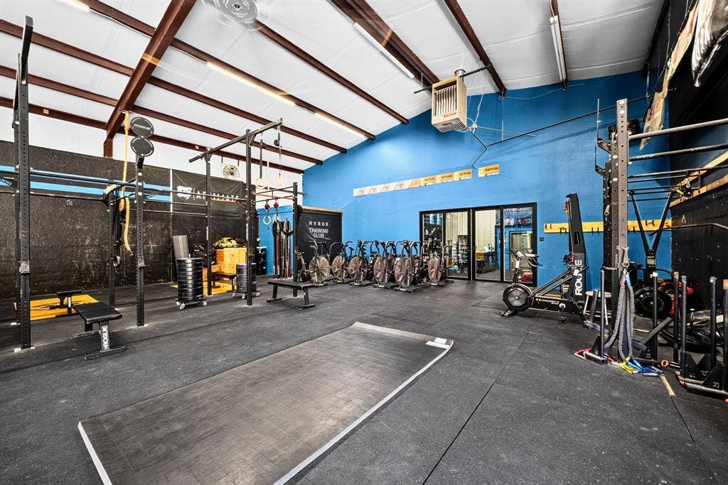 911 W Holiday Drive, Fate, TX 75132 High-ceiling recreational space featuring exposed structural steel, rubberized flooring, integrated wall-mounted heater, and glass-paneled entry doors