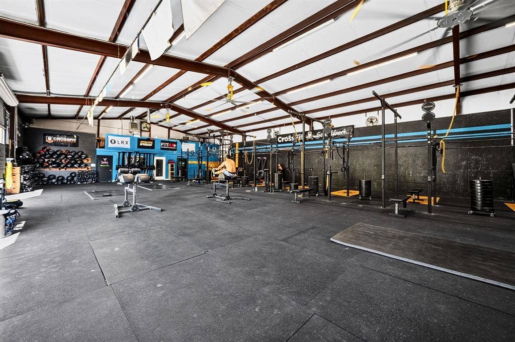 911 W Holiday Drive, Fate, TX 75132 Expansive open-concept space featuring vaulted ceilings with exposed steel beams, industrial lighting fixtures, and high-durability rubber flooring