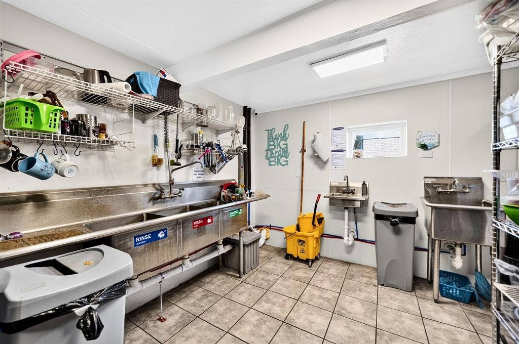 911 W Holiday Drive, Fate, TX 75132 Utility area featuring a multi-basin stainless steel commercial sink, a wall-mounted stainless steel utility basin, tile flooring, and integrated wire shelving