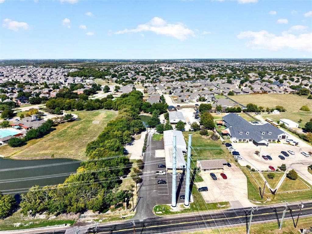 911 W Holiday Drive, Fate, TX 75132 Aerial perspective of the property featuring asphalt parking areas, multiple structures, established landscaping, and bordering water features