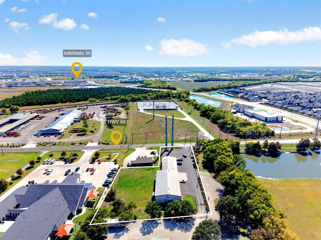 911 W Holiday Drive, Fate, TX 75132 Aerial view of commercial property featuring a metal-sided building, paved parking surface, mature perimeter trees, and highway proximity