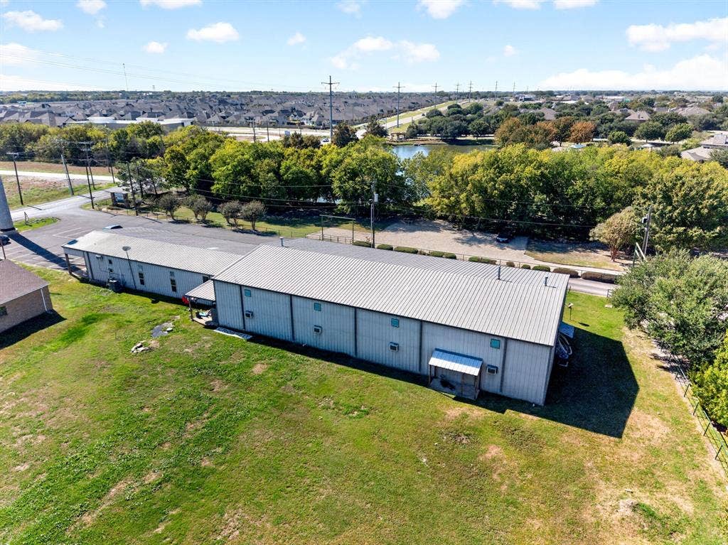 911 W Holiday Drive, Fate, TX 75132 Expansive metal-sided structure featuring a standing seam metal roof and a spacious lawn surrounding the building exterior