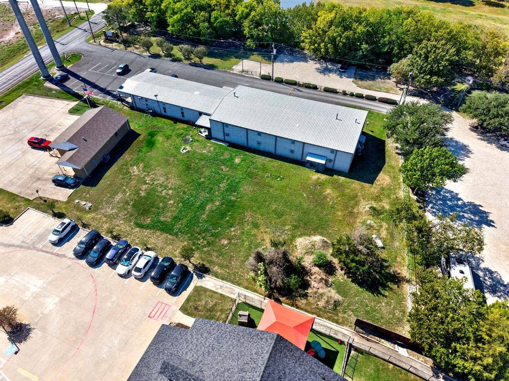 911 W Holiday Drive, Fate, TX 75132 Aerial perspective featuring multiple industrial structures, expansive open green space, paved parking areas, and mature perimeter trees