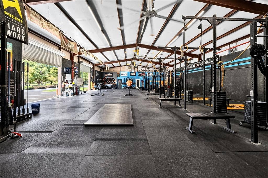 911 W Holiday Drive, Fate, TX 75132 Open-concept industrial space featuring a vaulted ceiling with exposed steel beams, high-capacity ceiling fans, recessed lighting, and durable rubberized flooring