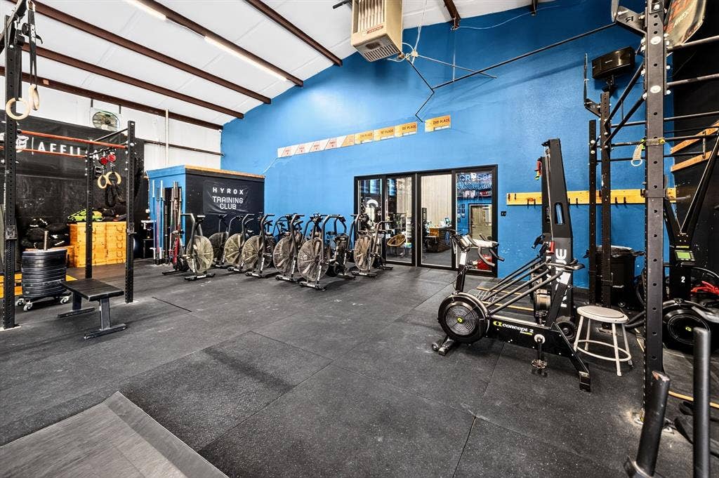 911 W Holiday Drive, Fate, TX 75132 Open-concept interior space featuring high vaulted ceilings, durable rubberized flooring, mounted industrial-style climate control unit, and extensive glass door entry