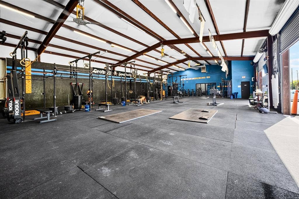 911 W Holiday Drive, Fate, TX 75132 Expansive open-concept interior featuring exposed metal trusses, high-clearance ceilings, durable rubber flooring, and a large roll-up metal bay door