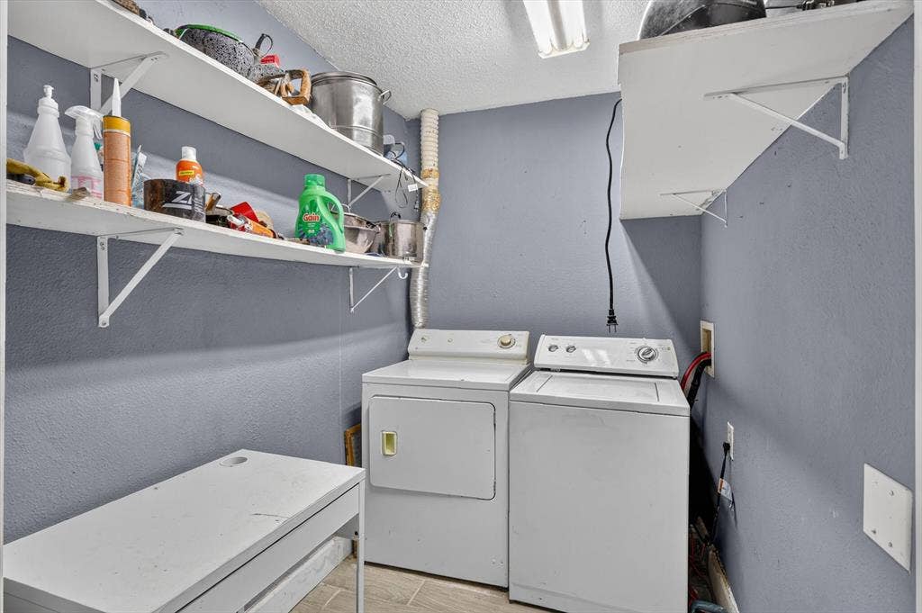 Laundry area featuring wall-mounted white shelving, tile flooring, and dedicated hookups for washer and dryer units