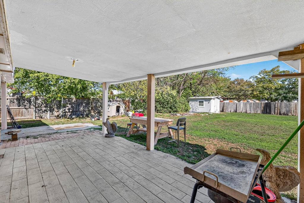 Covered patio featuring wood-finish tile flooring and support columns, expansive backyard, and perimeter wood fencing