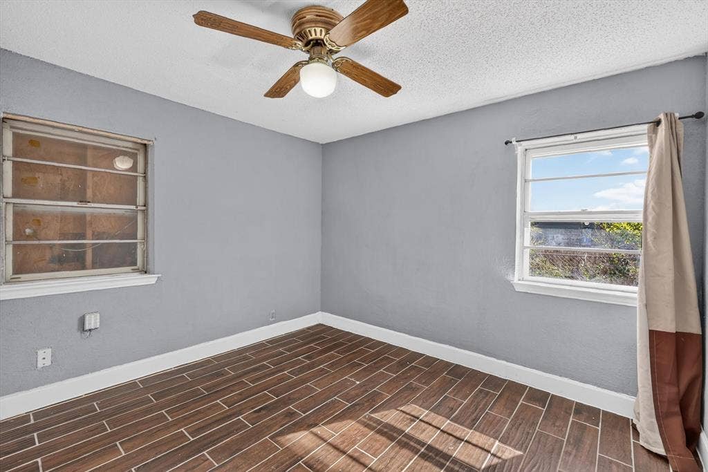 Interior space featuring wood-finish flooring, neutral gray wall paint, and a ceiling-mounted light fixture with an integrated fan