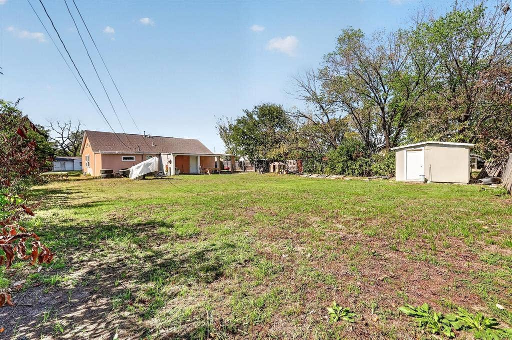 Expansive backyard featuring a large grass lawn, mature trees, and an exterior storage structure