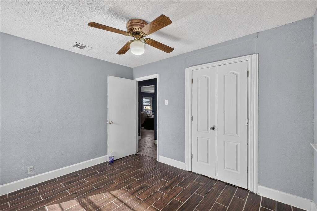 Wood-finish tile flooring, ceiling fan with light fixture, and white dual-panel closet doors