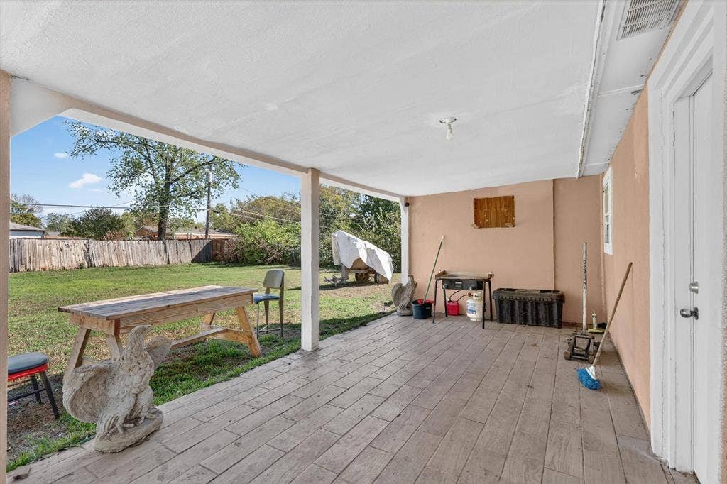 Covered patio featuring plank-style flooring and a grassy backyard enclosed by wood fencing