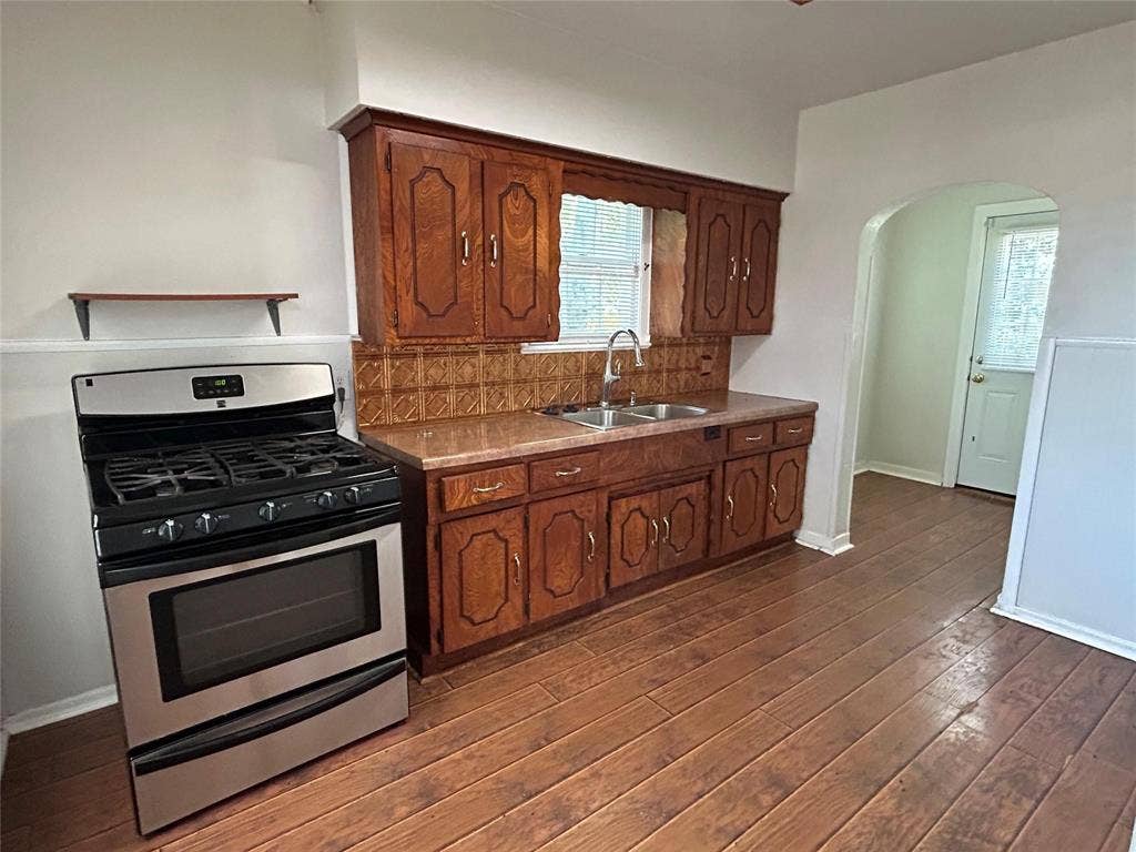 Kitchen featuring wood-finish cabinetry, a stainless steel gas range, a decorative metal backsplash, and a double-basin sink