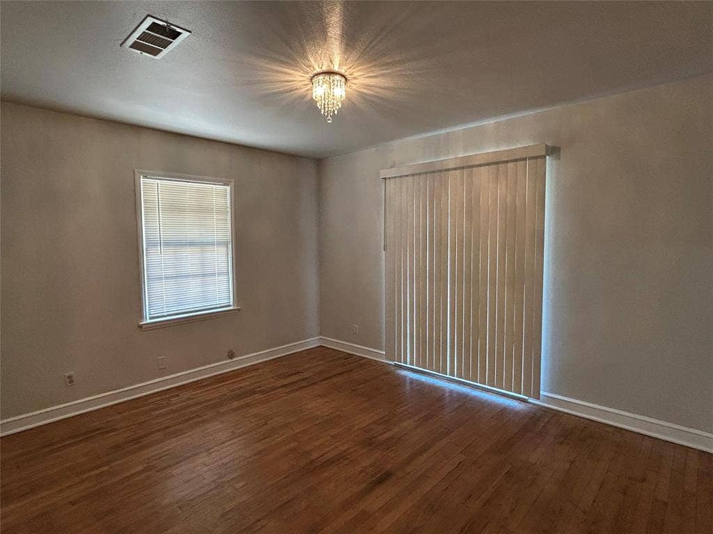 Hardwood flooring, crystal-style flush mount ceiling light fixture, sliding glass door with vertical blinds, and a single-pane window