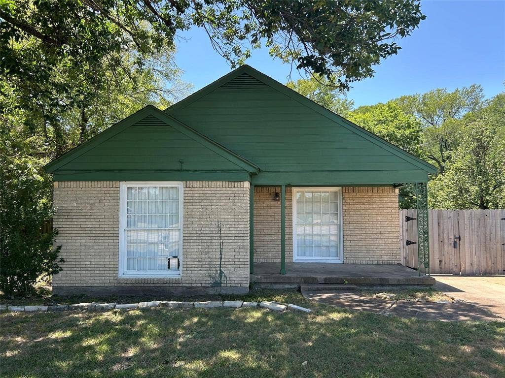 Single-story brick exterior featuring a covered front porch, gabled roofline, and wood-slat privacy fencing