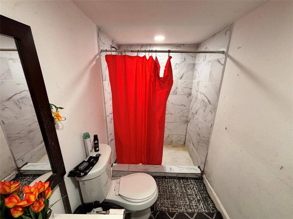 2917 Lenway Street, Dallas, TX 75215 Bathroom featuring a walk-in shower with large-format, light-toned stone-patterned wall tile and a built-in shower curb