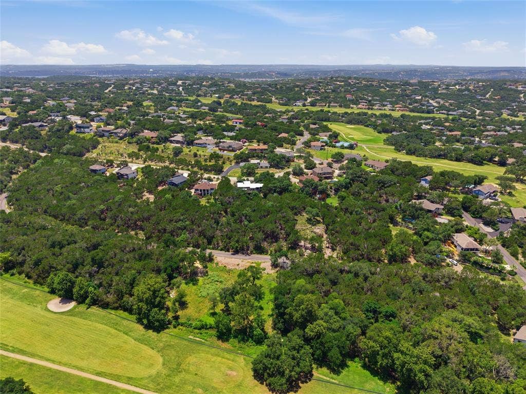 Aerial perspective showcasing a sprawling landscape featuring dense tree coverage, undulating terrain, open green space, and established residential development