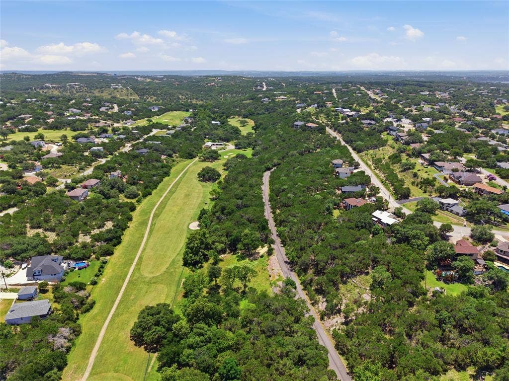 Aerial perspective showcasing a sprawling landscape with extensive native tree coverage, manicured grass fairways, and paved thoroughfares