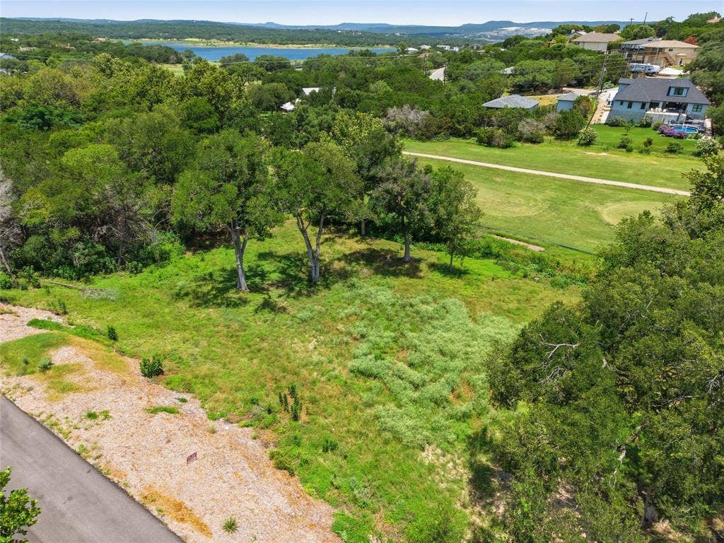 Expansive vacant lot featuring mature hardwood trees, natural topography, and asphalt road frontage, situated in a landscape with water features and distant hills