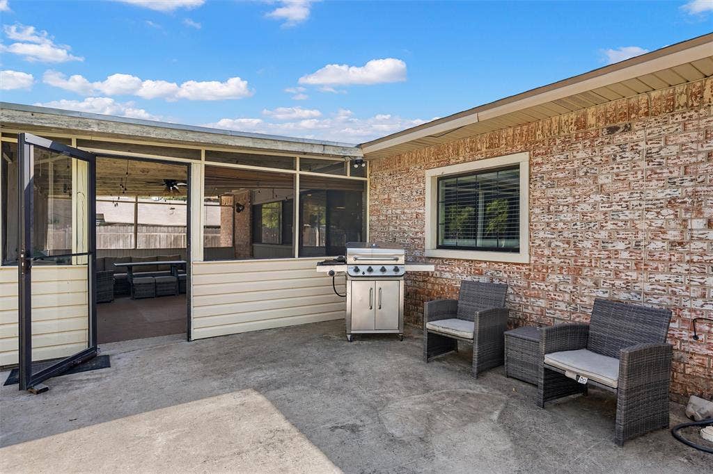 Concrete patio featuring a screened-in enclosure, brick exterior wall, and built-in window with white trim