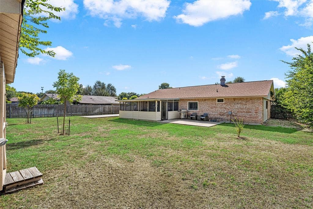 Backyard featuring a brick exterior, enclosed sunroom, concrete patio, and wood-panel perimeter fencing