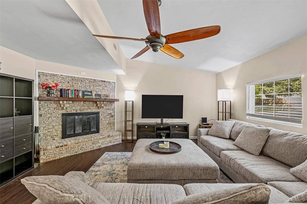 Living area featuring vaulted ceilings, wood-finish flooring, a stacked-stone fireplace with a timber mantel, and a five-blade ceiling fan