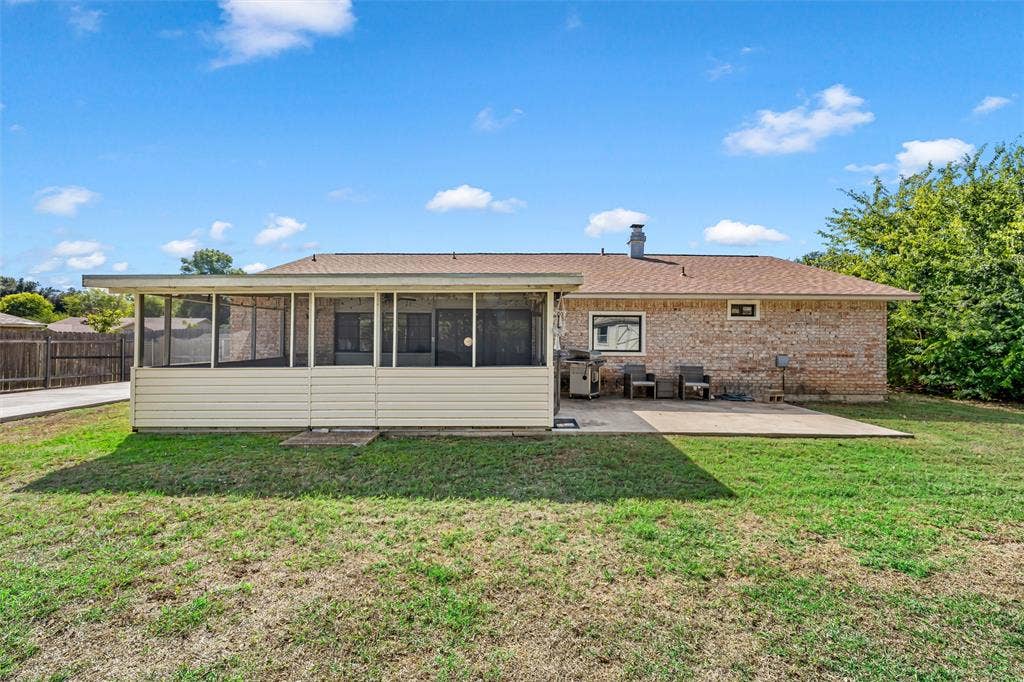 Rear exterior featuring a brick facade, screened-in porch with light-colored siding, concrete patio, and fenced backyard