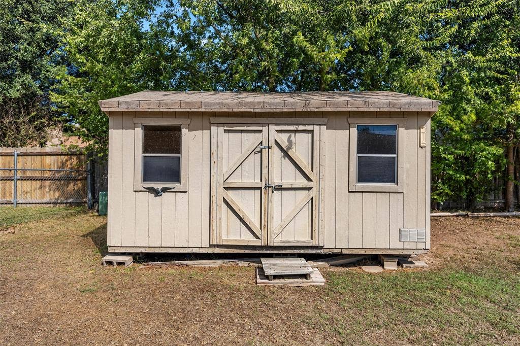 Outdoor storage structure featuring tan composite siding, two single-pane windows, double-door entry, and a pitched roof